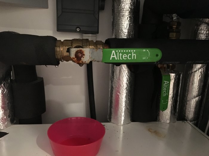 Isolerade rör med kondens och rost samt en rosa skål som samlar upp vattendroppar under rören.