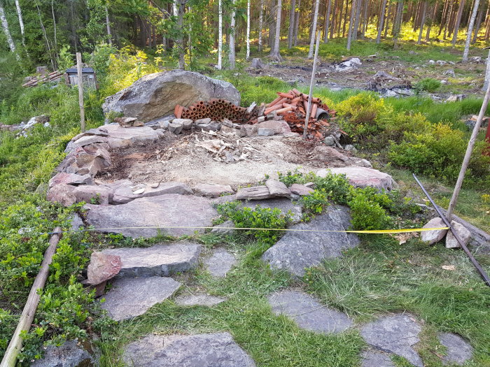 Förberedd plats för gjutning med stenar, singel, och mätinstrument på ett byggprojekt i skogsmiljö.