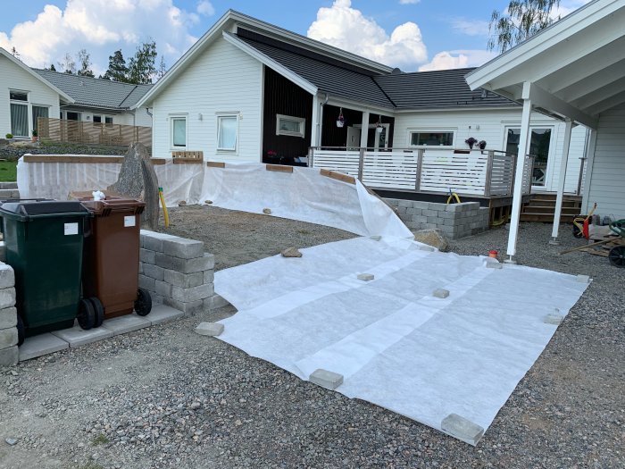 Byggprojekt med markduk och stenmur, förberedelse för leverans av matjord i trädgård.