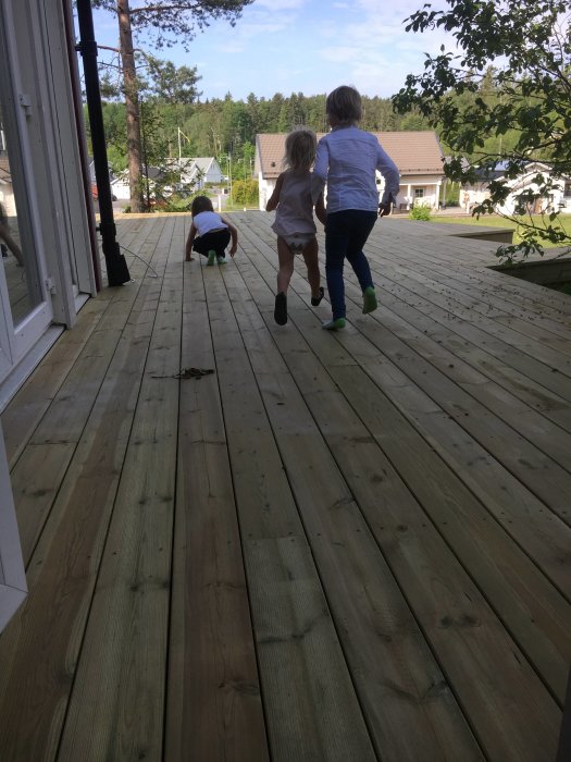 Barn springer på nybyggd träaltan med bostadshus i bakgrunden.