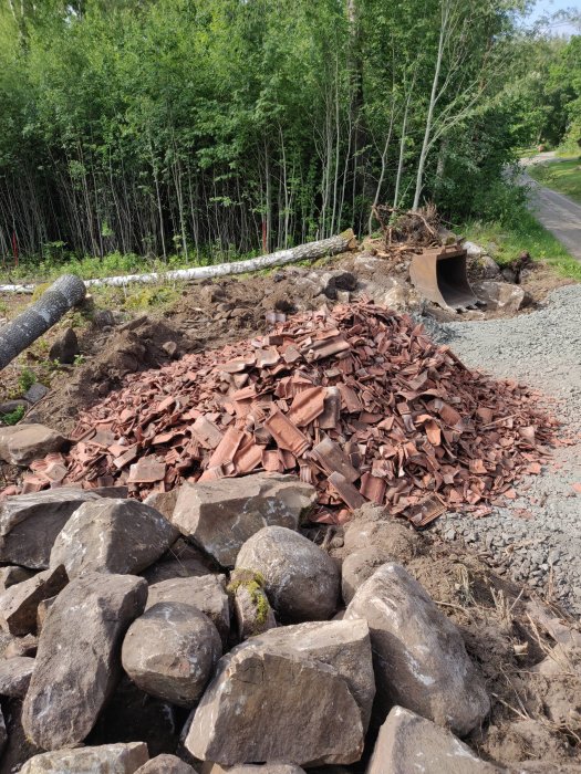 Nygrusad parkeringsplats med en hög brunröda takpannor och stenar i förgrunden, med grönska i bakgrunden.