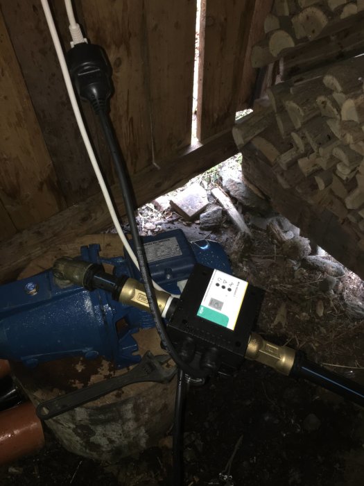 Vattenpump och tryckregulator i skjul med synlig vit strömkabel och sugslang.