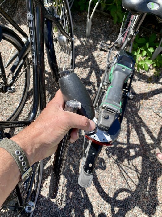 Hand håller en batterivinkelslip med synliga användningsspår nära en cykel.