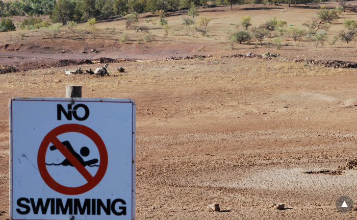 No Swimming"-skylt framför en uttorkad damm, symboliserar effekten av lokala klimatförändringar.