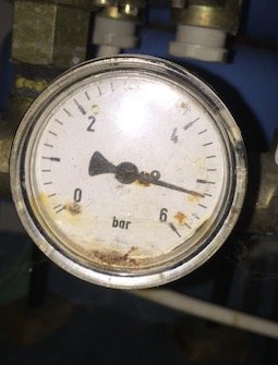 Smutsig manometer visar över 5 bar tryck, kopplad till vattensystem.