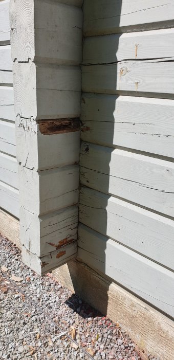 Något skadad träpanel på ett hus med flagande färg och tecken på röta vid ett hörn.