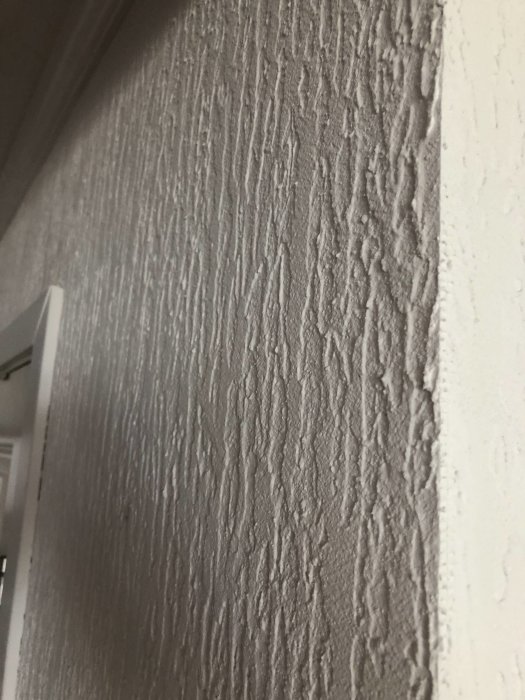 Närbild av en vägg med grov struktur som inte verkar vara tapet, möjlig byggskiva eller panel.