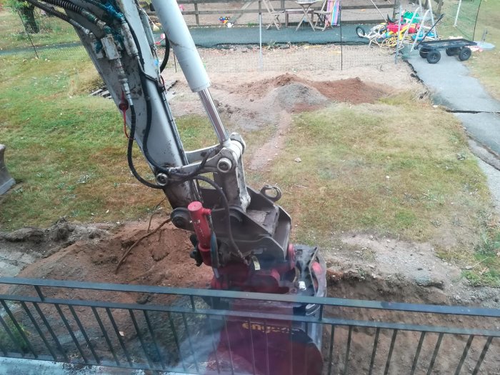 Utsikt från ett fönster på en grävmaskin som arbetar med att gräva upp en trädgård med leksaker och en skateboardramp i bakgrunden.