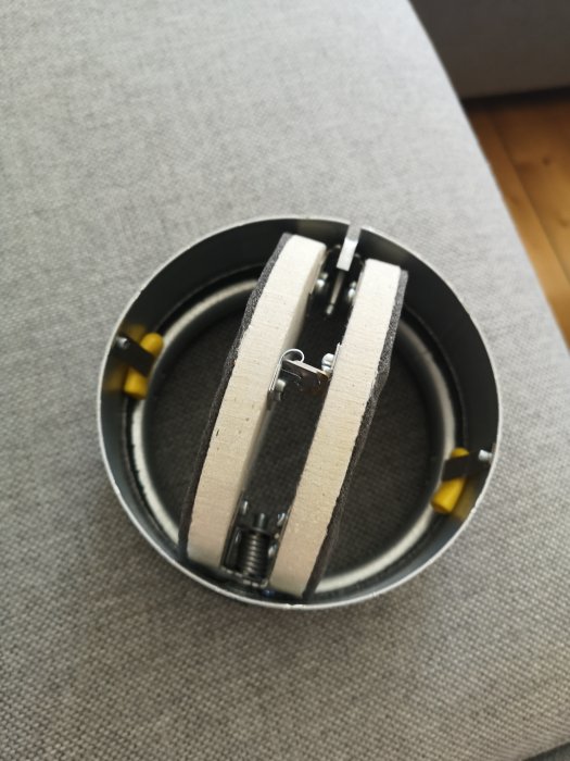 Brandspjäll i metall med gula fästelement och fjädermekanism, mot grå bakgrund.