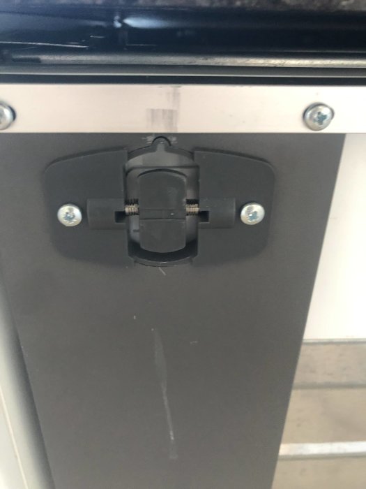Söndrad plastglidhållare i nedre delen av en öppen diskmaskinslucka med synliga skruvar och en skena i mitten.