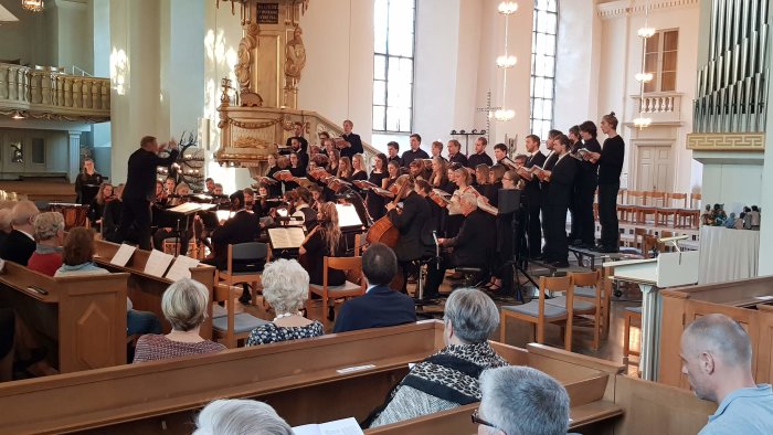 Kör och orkester framträder i kyrka med dirigent och publik.