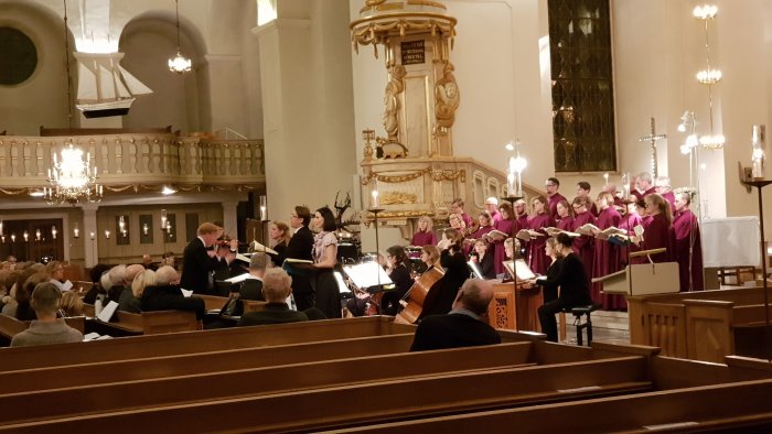 Orkester och kör uppträder i en kyrksal med publik i förgrunden.