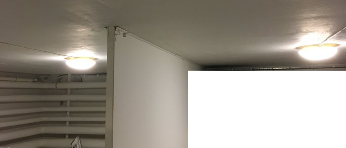 Källarbelysning med två plafonder på lågt tak och synliga rör och kablar.