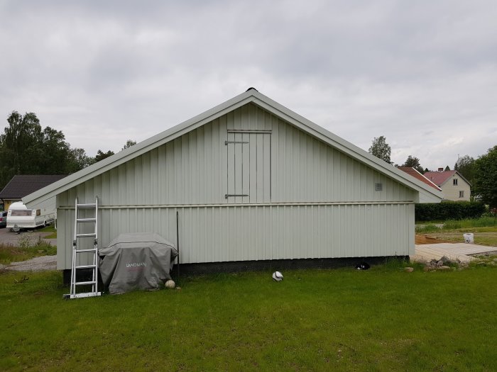 Nyrenoverat grått hus med spetsigt tak och stege lutad mot ena gaveln, omgivet av gräsmatta.