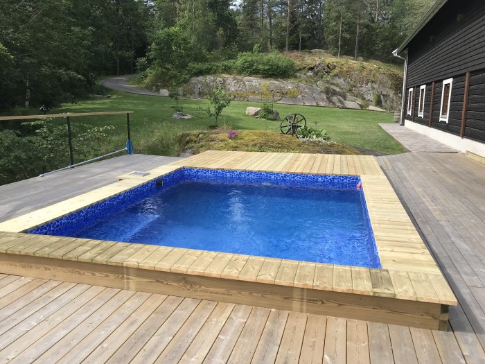 Nybyggd ovanmarkspool med vatten, inbäddad i trädäck vid en villa med grönskande trädgård.