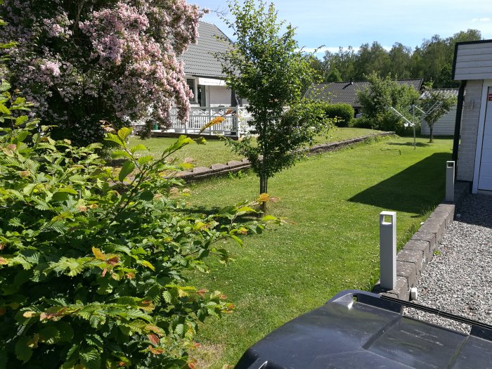 Gammal låg stödmur av sten längs med en trädgård nära en villa, synliga tecken på förfall och ojämn höjd.