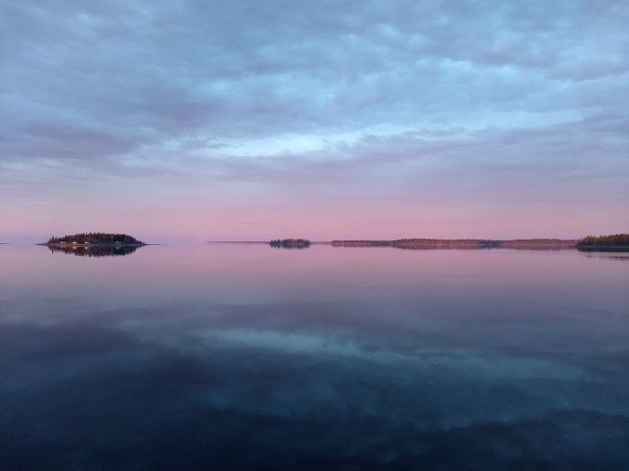 Rosa och blå himmel i juninatt speglar sig i lugnt vatten i Norrland med silhuetter av öar.