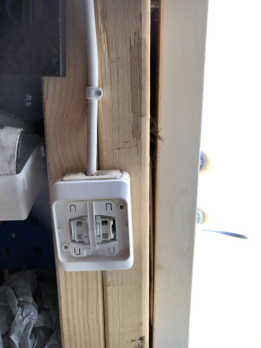 Dubbel vägguttag installerad på en trävägg med elkabeln ansluten ovanifrån.