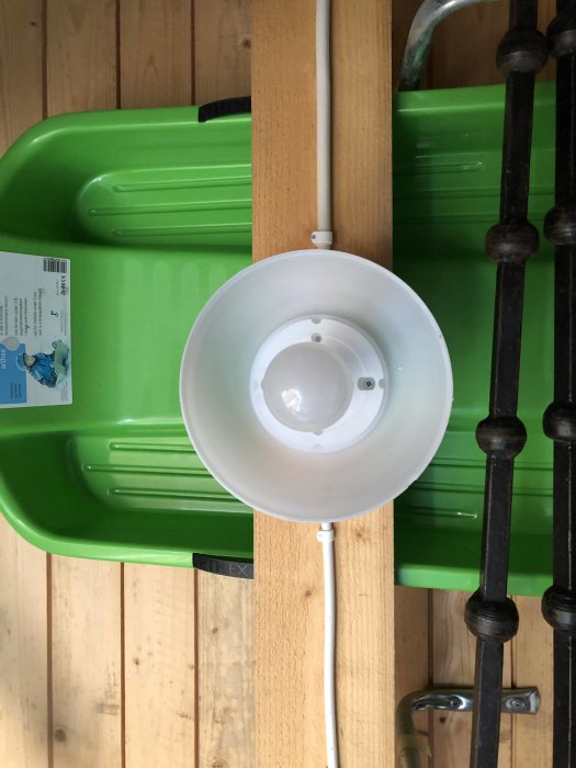 En taklampa och en sladd som leder till en strömbrytare, med en grön plastback och trävägg i bakgrunden.