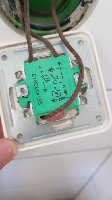 Öppnad eluttagsskåpa med en grön kabelkopplingsplint, tre bruna kablar och ett schematiskt diagram, sedd uppifrån.