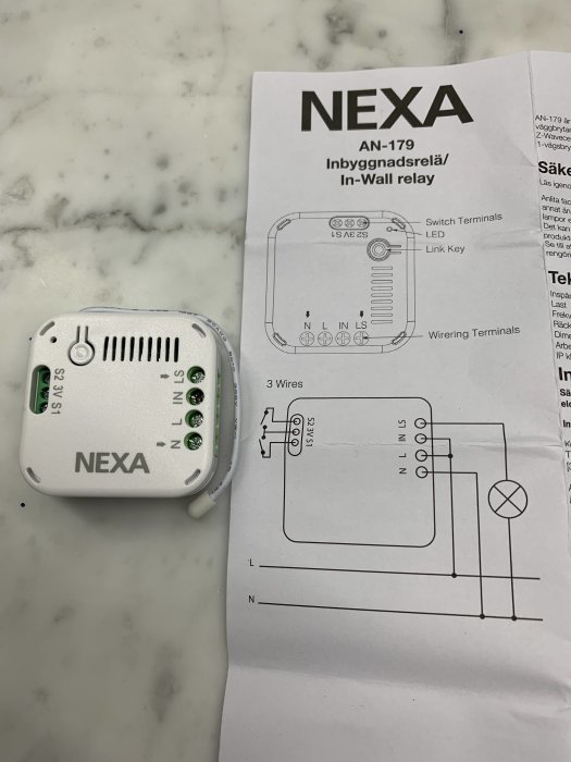 Nexa AN-179 inbyggnadsrelä bredvid dess installationsmanual på en marmorbänk.