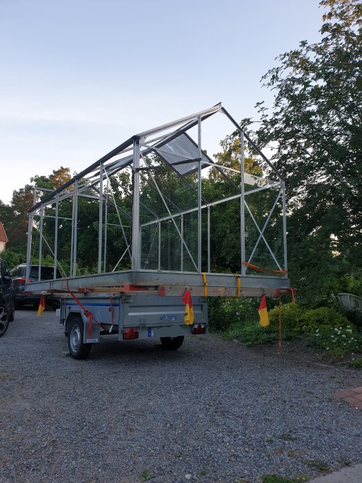 Ett demonterat växthus laddat på en släpvagn parkerad på en grusdriveway under kvällen.