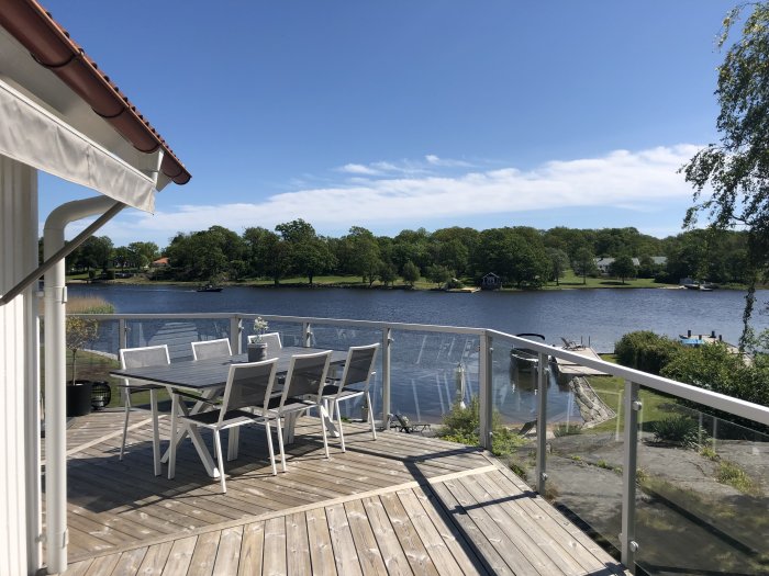 Utsikt över vattnet från träaltan med matbord och stolar, under en klarblå himmel.