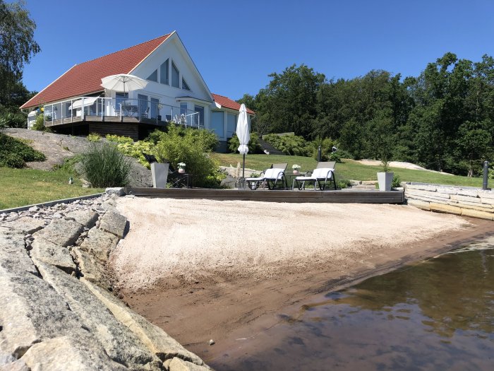 Vit villa med röd tak och en veranda, angränsande till strand och vatten i en skärgårdsmiljö.