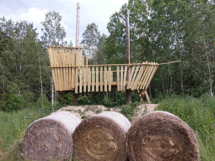 Trappa och delvis färdigt trä-räcke till en påbyggd konstruktion i naturmiljö med höbalar i förgrunden.