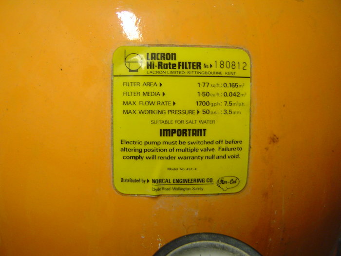 Informationsetikett på en poolfiltertank med tekniska specifikationer, visande åldern på filtret och möjlig behov av underhåll.