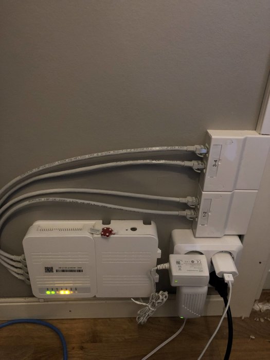 En fiberanslutningsbox med ethernetkablar, vägguttag och ansluten nätadapter.