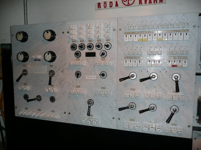 Kontrollpanel från biografmuseet med vred och mätare på marmorskiva, skylt "RÖDA KVARN" i bakgrunden.