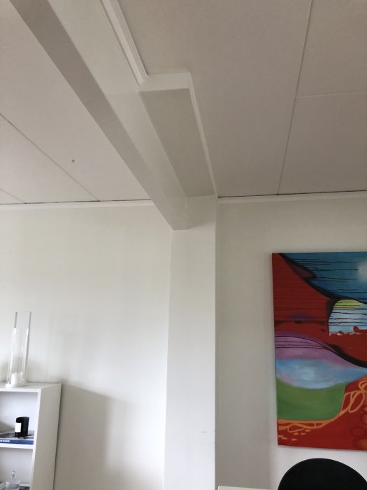 Bild på en vit bjälke i taket som fortsätter ned längs en vägg i ett rum med ett färgglatt måleri.