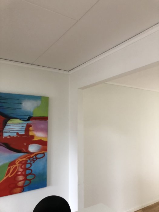 Hörn av ett rum med öppet takstom och en färgglad tavla på väggen.