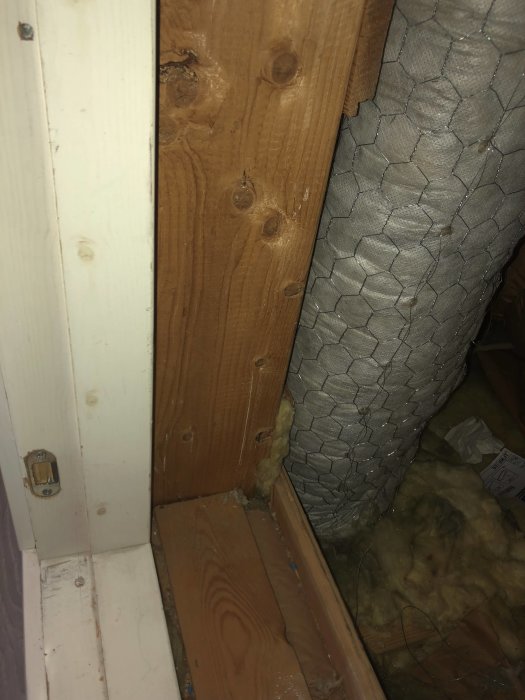 Ventilationsrör nära dörrtröskel till kallvind med isolering och synligt träarbete.
