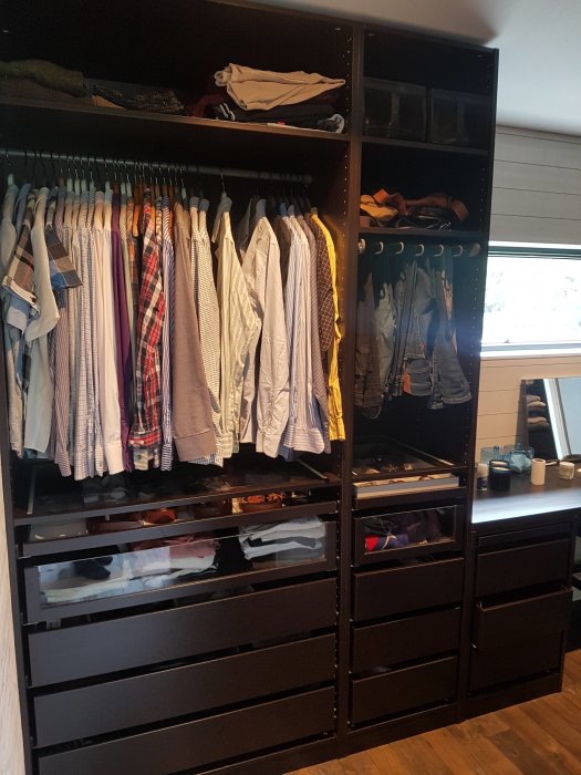 Nyinredd garderob med öppna dörrar som visar skjortor på galgar, hyllor med kläder och lådor med vikta plagg.