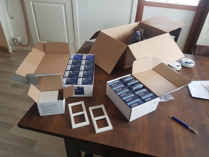 Installationsmaterial för KNX-system på ett bord med öppnade kartonger, ramverk och verktyg.