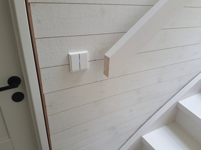 Nyinstallerad KNX-styrpanel vid trätrapp och vitmålad vägg i ett nyrenoverat hem.