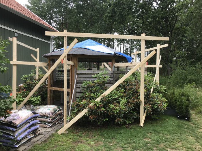 Ofärdig träkonstruktion med presenning på taket och byggmaterial på marken.