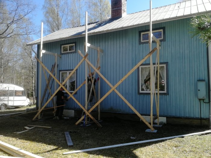 Byggställning av trä runt en blå träfasad under takrenoveringsarbete med person som arbetar.