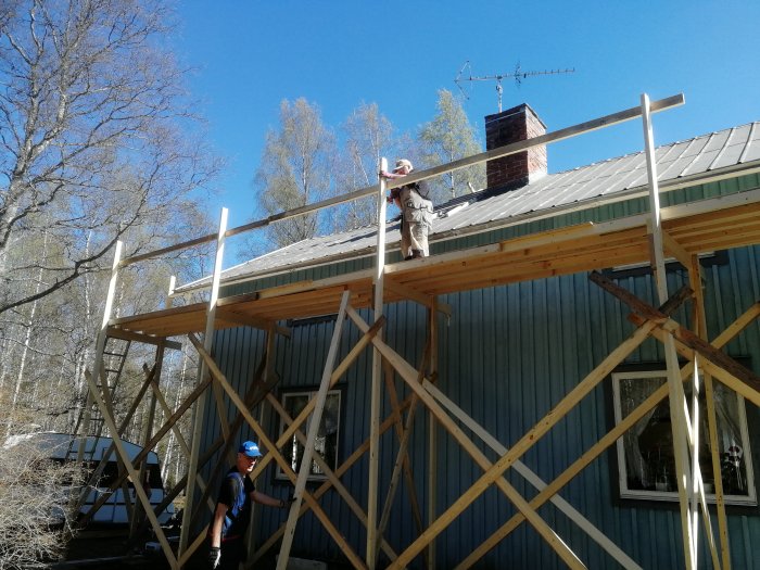 Personer arbetar på träställning vid takrenovering på ett hus.