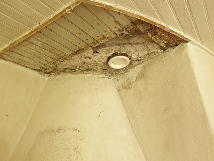 Skadat takhörn med exponerade träbjälkar och mögel ovanför en kamin i en stuga.