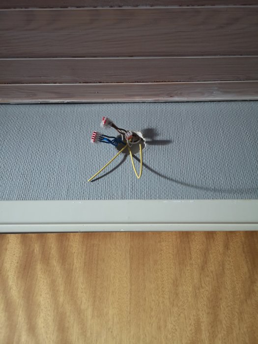 Elektriska kablar som sticker ut från en vägg nära golvet, med en delvis monterad uttagsdosa.