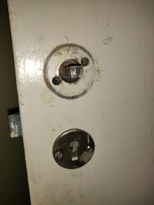 Nedsliten dörr med gammal nyckelhål och vredmekanism som behöver renovering.