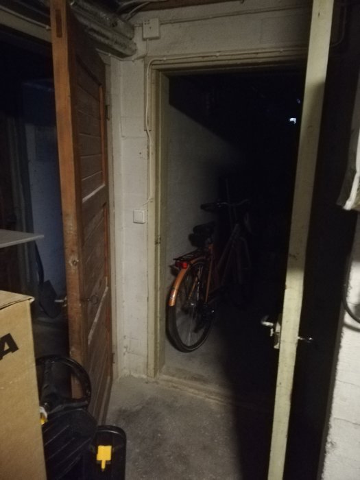 Mörk bild på ett renoveringsprojekt med betongväggar och en dörröppning, cykel i bakgrunden.