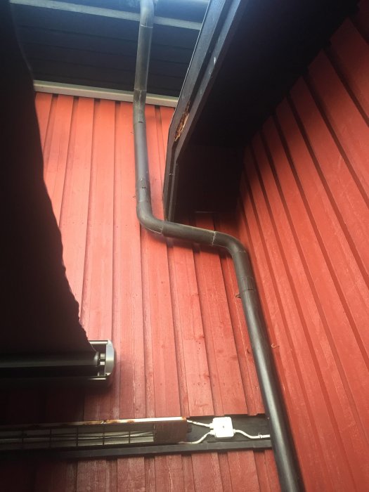 Rostig infravärmare monterad på röd vägg under takutsprånget med synliga elledningar och väggdosa.