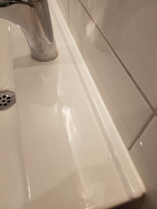 Närbild på ny fogad skarv mellan handfat och kakelvägg i badrum.