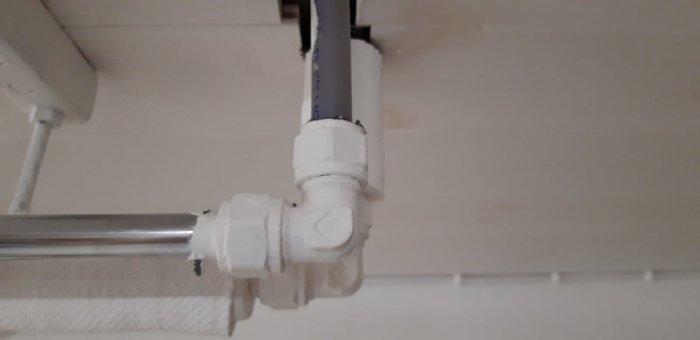 Vattenledningar med vinkelkoppling och T-koppling i ett rörsystem under tak, klämringskopplingar synliga.