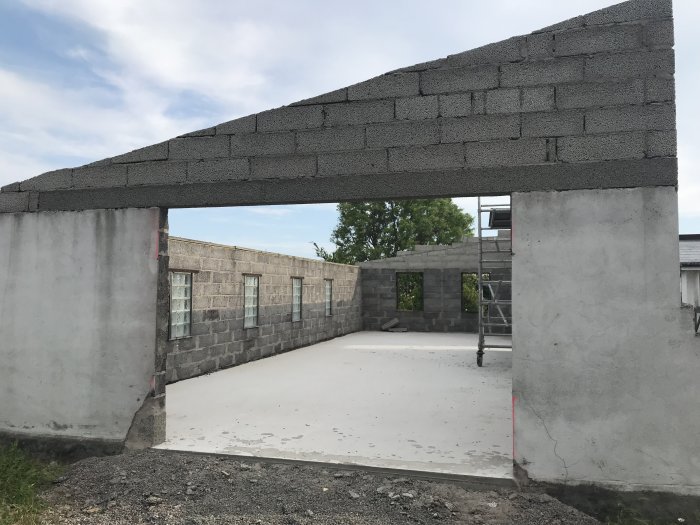 Nyinstallerad balk över öppning i garagebygge med hammarband redo för takreglar, grå betongblockväggar och betonggolv.