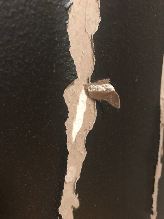 Skadad gipsvägg med limrester och avsliten kartong efter borttagning av bröstpanel.